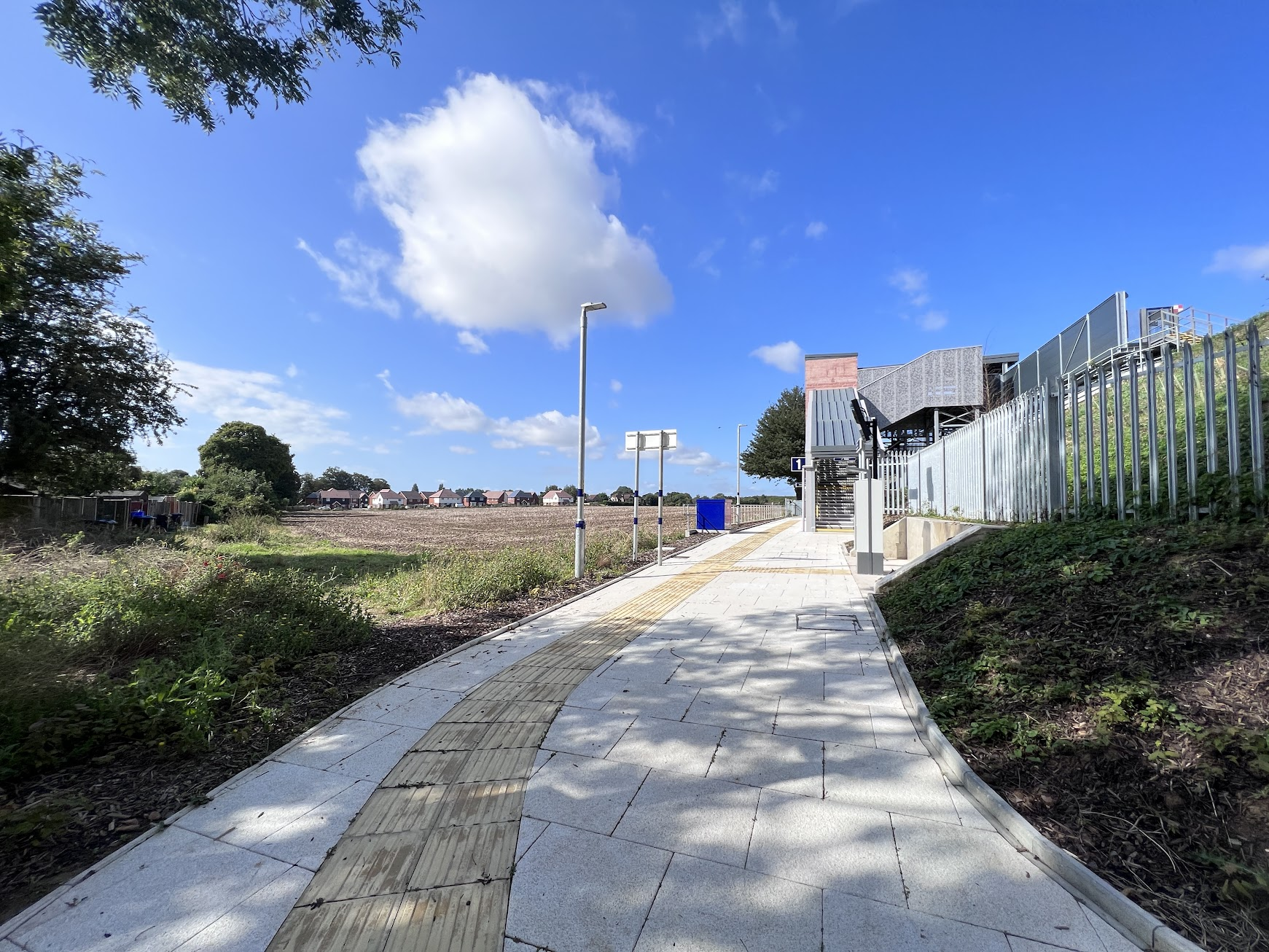 New railway station next to fields with houses in distance.