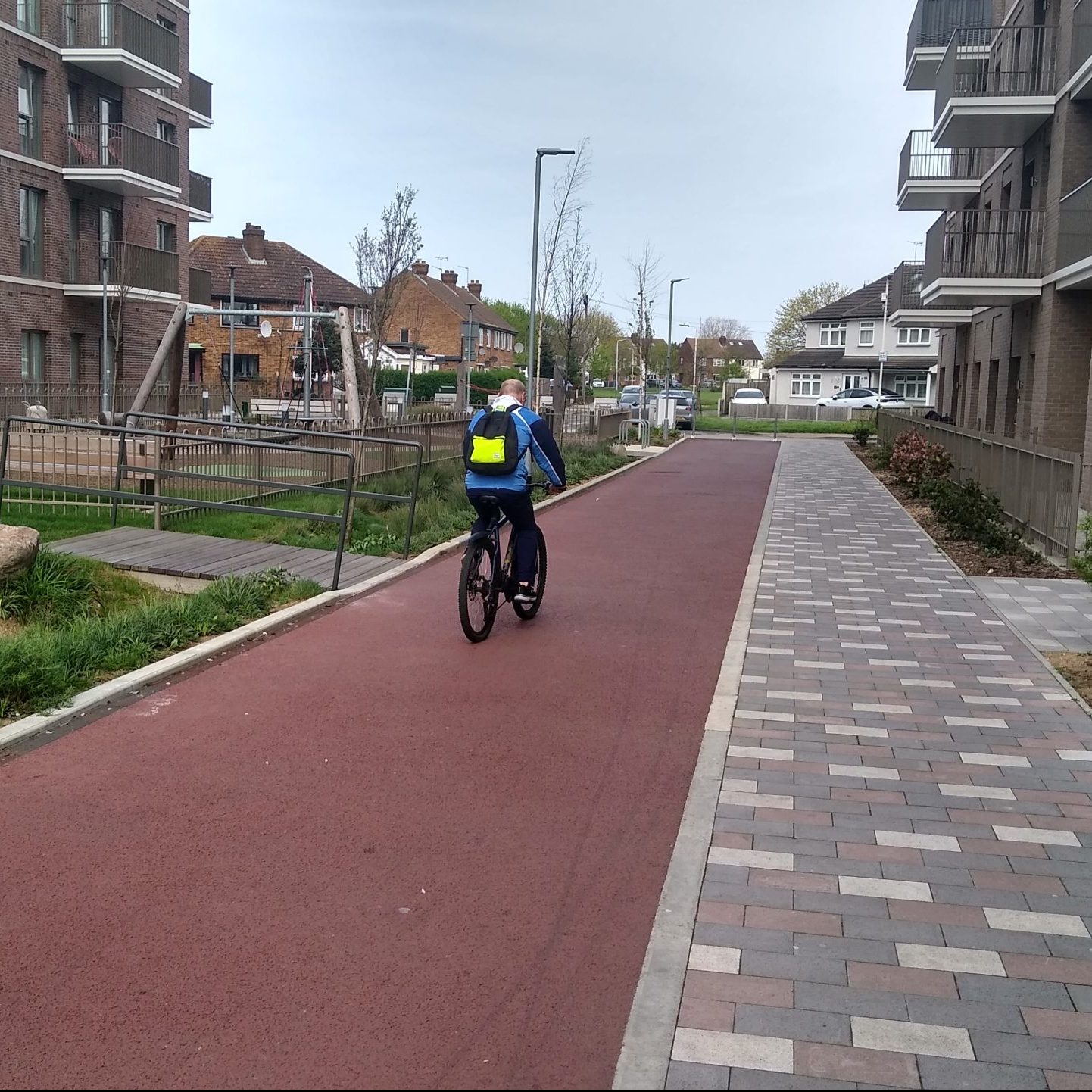 Cyclist on cycle tracks between modern flats with houses in background.